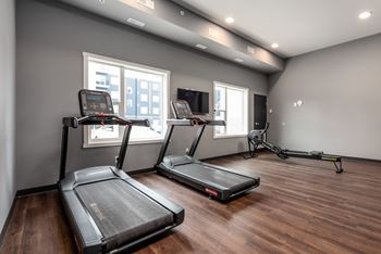 two treadmills in a room with two windows and a tv
